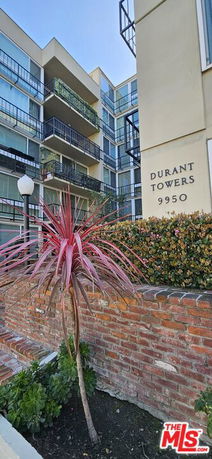 Front view of a multi-story building with balconies and a brick wall in the foreground.