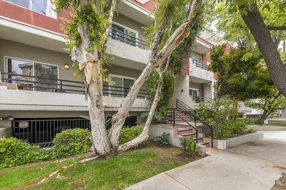 Front view of a multi-story residential building with balconies and stairs, surrounded by trees.
