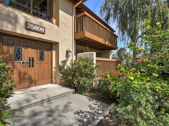 Front view of a two-story house with a balcony and brown double doors.
