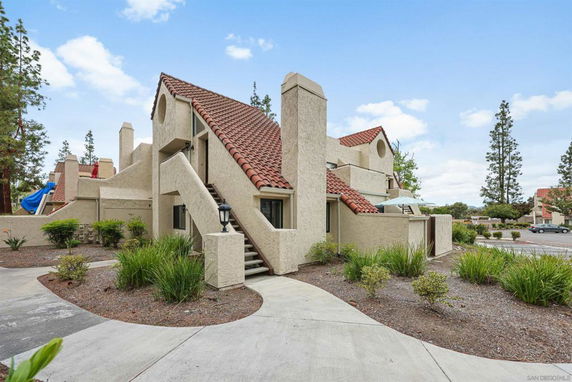 View of a multi-story building with beige stucco walls and red tile roof.