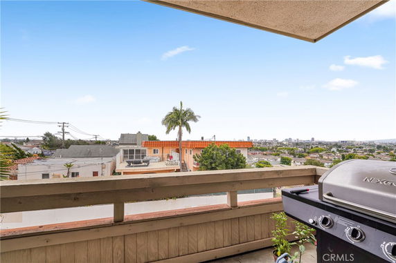 View from a balcony overlooking residential and cityscape area, with a barbecue grill in the foreground.