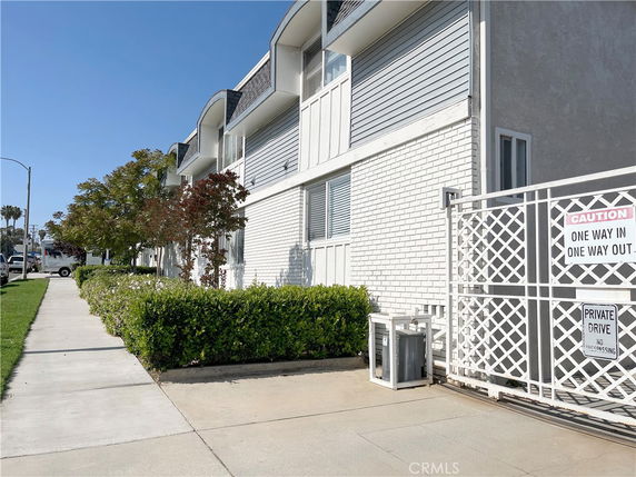 Side view of a multi-story building with white brick exterior and gated entrance.