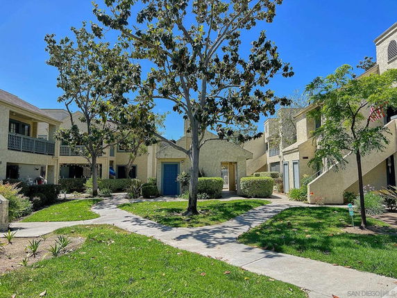 View of multiple two-story apartment buildings with trees and walkways in an outdoor setting.