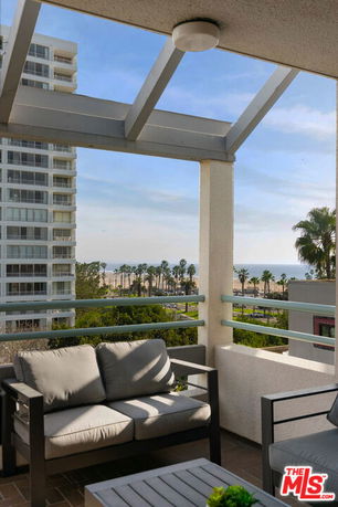 View from a balcony showing a neighboring high-rise building and a distant beach with palm trees.