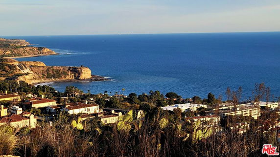 Panoramic view of the coastline and ocean, with buildings and vegetation in the foreground.
