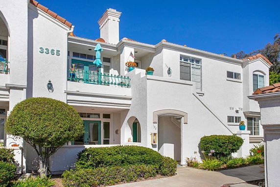 Front view of a white two-story house with a balcony and potted plants.
