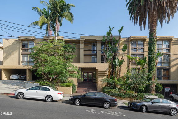 Front view of a multi-story apartment building with balconies and parking spaces.