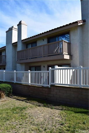 Front view of a two-story building with balconies and a white fence.