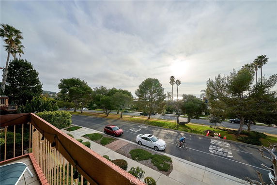Panoramic view of a street with trees and parked cars from a balcony.
