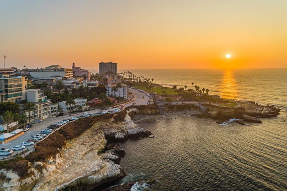 Panoramic view of a coastal cityscape at sunset with ocean and buildings.