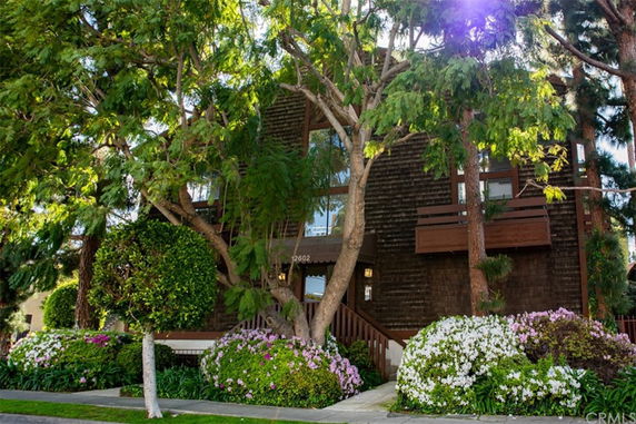 Front view of a multi-story building with wooden exterior and balconies, surrounded by trees and shrubs.