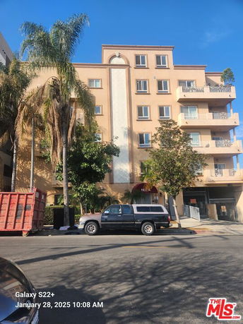 Front view of a multi-story residential building with balconies and palm trees.