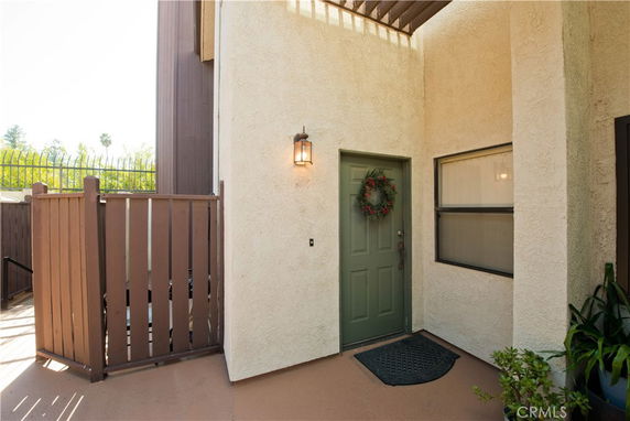 Entrance view of a building with a green door and light fixture, partially enclosed by a wooden fence.