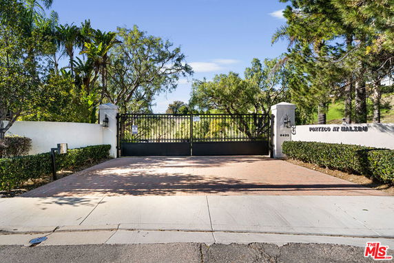 View of a gated entrance with white walls and greenery.
