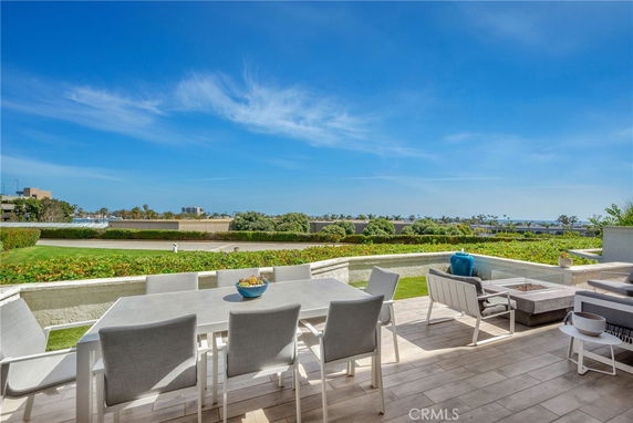 Outdoor patio with dining table overlooking a landscaped area and distant views of buildings and water.