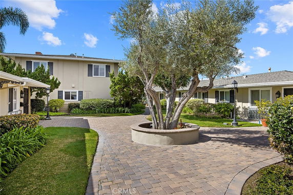 Front view of multiple-story house with tiled walkway and tree planter in foreground.