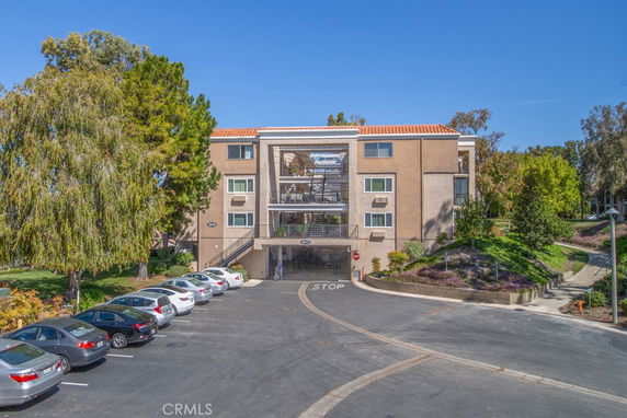 Front view of a three-story apartment building with a central open staircase and parking area.