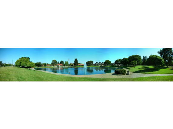 Panoramic view of a park with a large pond and fountain.