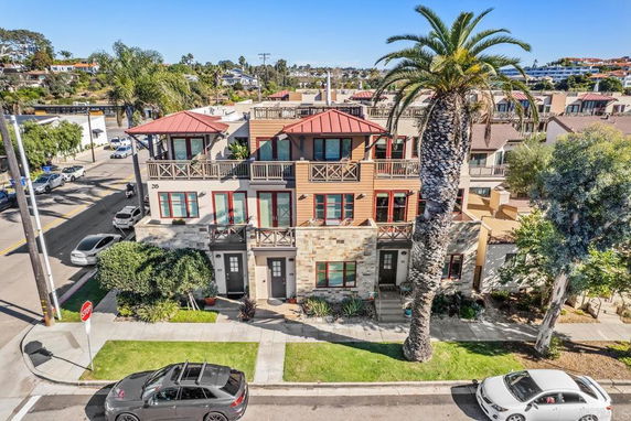 Front view of a multi-story house with balconies and palm trees.