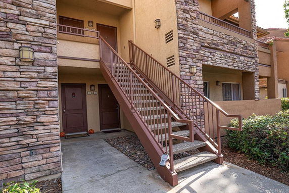 Front view of a residential building with stone and stucco exterior, featuring stairs leading to the upper floor.