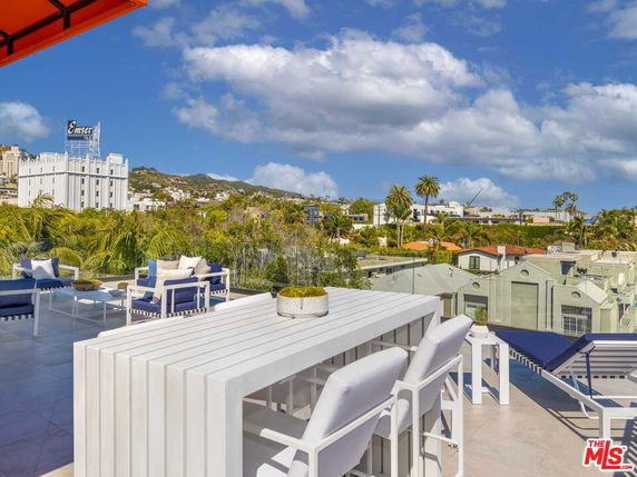 Panoramic view from a rooftop with outdoor seating, overlooking cityscape and hills.