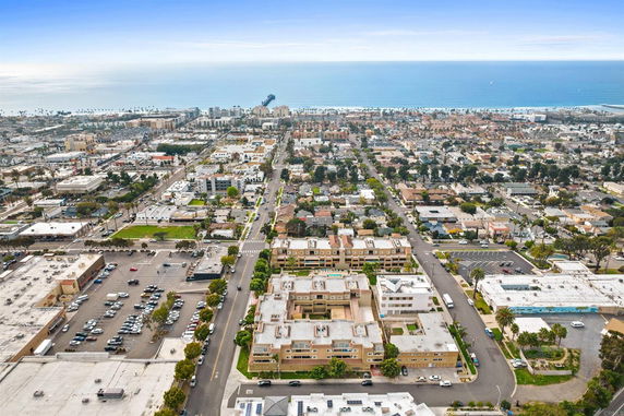 Aerial view of an urban area with residential and commercial buildings, roads, and the ocean in the background.