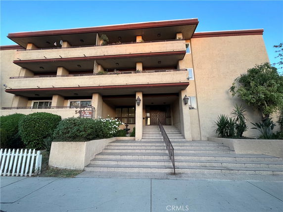 Front view of a multi-story building with balconies and staircase entrance.