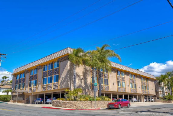 Front view of a multi-story building with large windows and covered parking area.