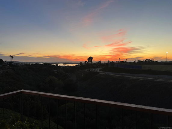 Panoramic view of the landscape at sunset from a balcony, overlooking a road and distant water.