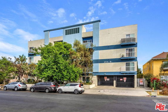 Front view of a multi-story building with balconies and a gated parking area.