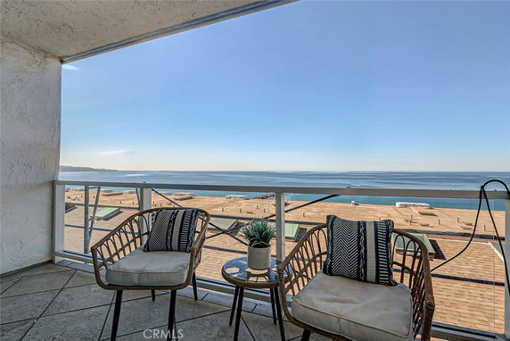 Panoramic view of the ocean from a balcony with chairs and a small table.