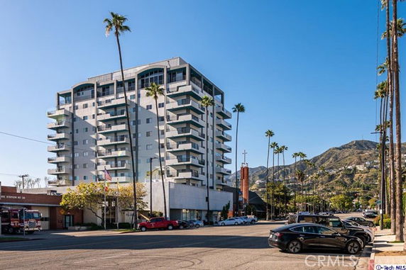 Front view of a multi-story building with balconies and palm trees around.