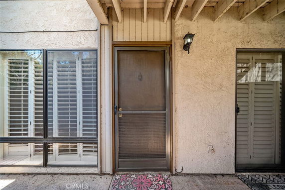 Front view of a building entrance with a screen door and windows with shutters.