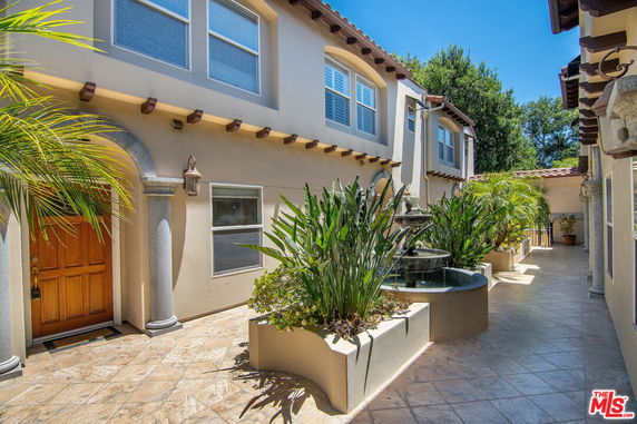 Front view of a two-story house with arched doorway and plants along the walkway.