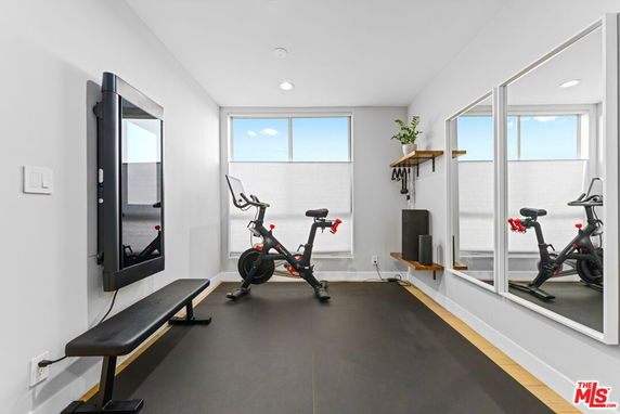 Home gym area with exercise bike, wall-mounted TV, and mirror.
