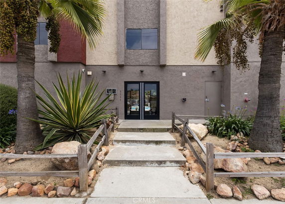 Front view of an apartment entrance with plants and a walkway.