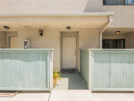 Front view of a building entry with a light-colored door and a small fenced patio area.