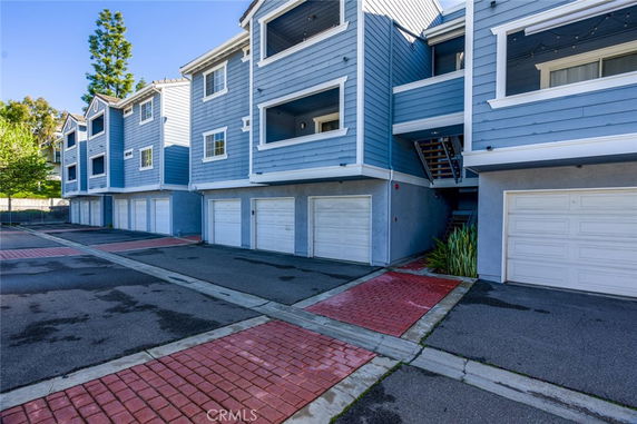 Front view of a multi-story townhouse with blue siding and white garage doors.