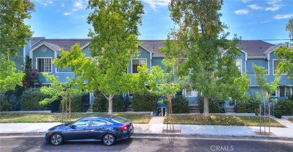 Front view of a two-story townhouse with trees in front and a parked car on the street.