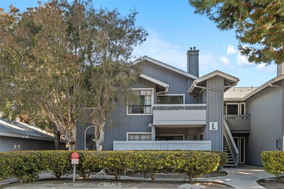 Front view of a two-story house with a balcony and trees surrounding the structure.