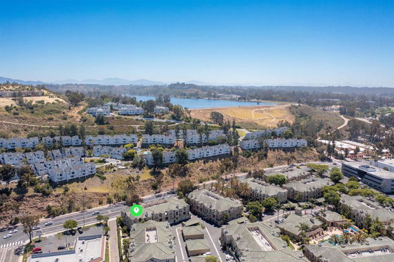 Aerial view of residential area with multiple housing units and natural surroundings including a body of water and hills.