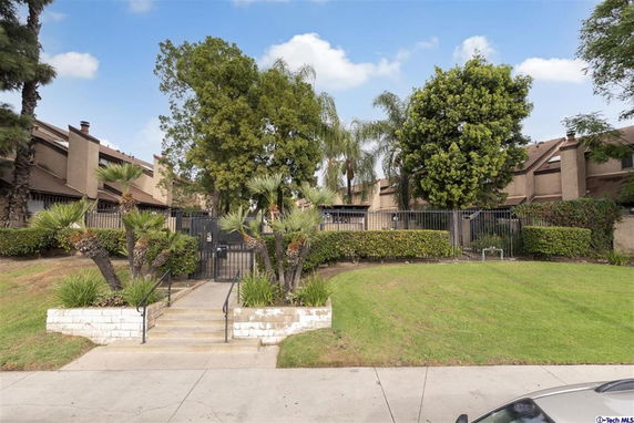 Front view of a multi-story residential building with a gated entrance and surrounding trees.