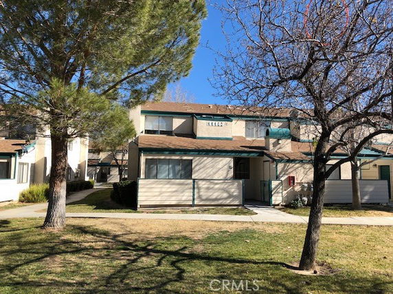 Front view of a two-story residential building with a brown roof and trees in the foreground.