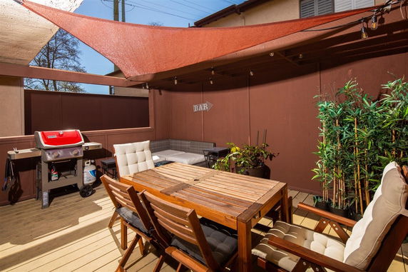 Outdoor patio area with wooden dining table, chairs, grill, and shade sail.
