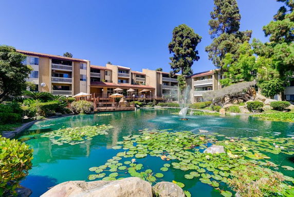 Front view of a multi-story building with large windows and a lush pond in the foreground.