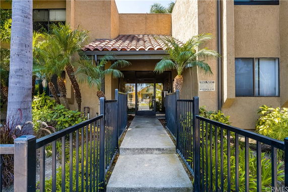 Front view of a building entrance with a tiled roof and surrounding plants.