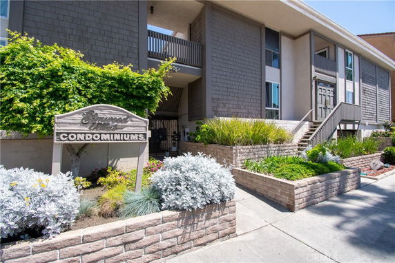 Front view of a condominium building with a sign and landscaped garden.