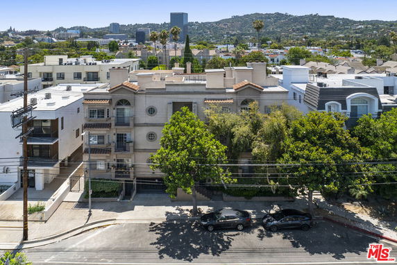 Front view of a multi-story apartment building with balconies and surrounding trees.