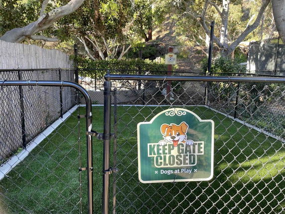 Enclosed outdoor play area for dogs with a sign on the gate.