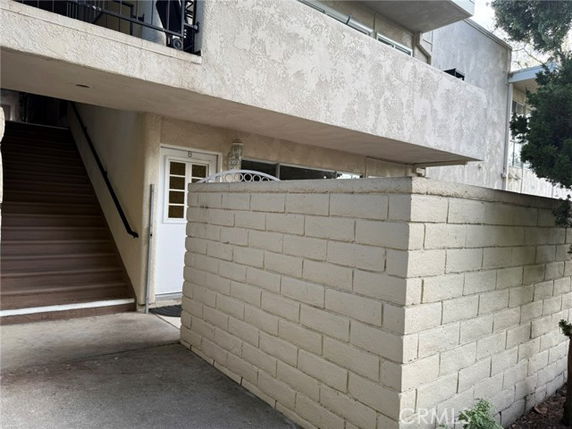 Front view of a multi-story building with stairs and a white door on the ground floor.